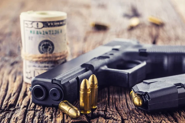 Zbraň a peníze. 9 mm pistole pistole odrážky rozházené a roll dolarové bankovky na rustikální dubový stůl — Stock fotografie