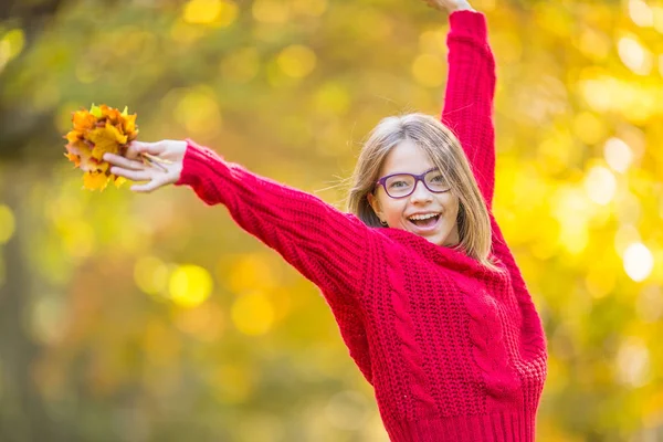 Gelukkig val herfstbladeren meisje lachende en blije bedrijf. Mooi jong meisje met esdoorn bladeren in de rode vest — Stockfoto