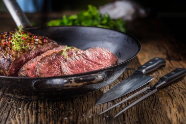Sığır eti biftek. Sulu orta kaburga biftek dilimlerini çatal ve bıçak otlar baharatlar ve tuz ile ahşap tahta üzerinde tava