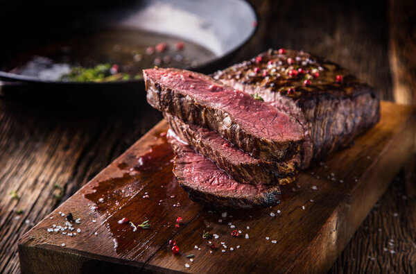 Beef steak. Juicy medium Rib Eye steak slices on wooden board with fork and knife herbs spices and salt.