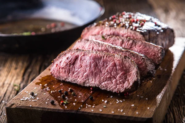 Rindersteak. saftige mittelgroße Rib-Eye-Steakscheiben auf Holzbrett mit Gabel und Messer Kräuter Gewürze und Salz — Stockfoto