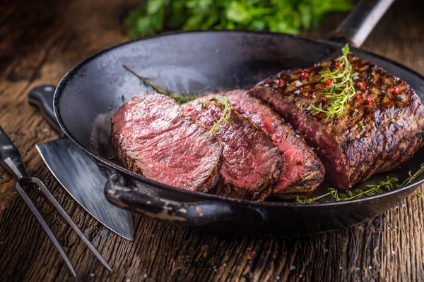 Sığır eti biftek. Sulu orta kaburga biftek dilimlerini çatal ve bıçak otlar baharatlar ve tuz ile ahşap tahta üzerinde tava