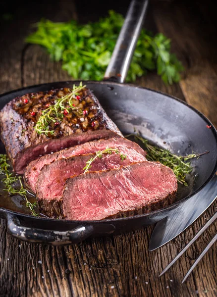 Biefstuk. Sappige middellange Rib Eye steak plakjes in de pan op een houten bord met mes en vork kruiden specerijen en zout — Stockfoto