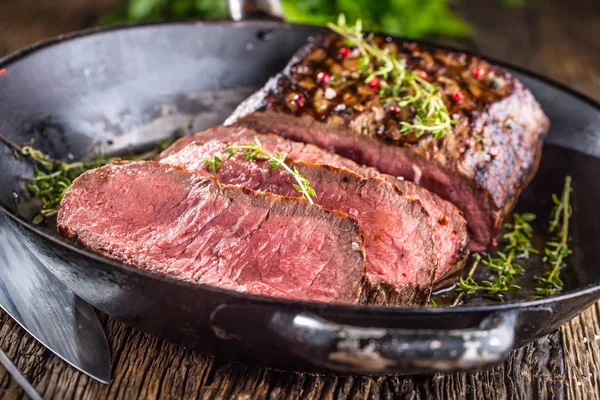 Bife de vaca. Suculento médio costela Olho fatias de bife na panela em tábua de madeira com garfo e faca ervas especiarias e sal — Fotografia de Stock