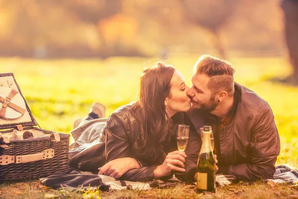 Ung härlig glad par - älskare har en picknick i höst park. Lyckligt par spottar och kyssas med glas champagne — Stockfoto