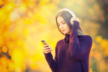 Akıllı telefon dinleme müzik sonbahar Park ve kulaklık ile mutlu genç kız portresi