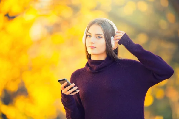 Portret szczęśliwy młoda dziewczyna z słuchawki i smartphone słuchania muzyki w jesienny park — Zdjęcie stockowe