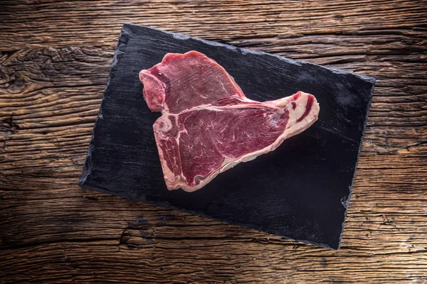 Nötstek T-bone. Rå biff T-bone skiffer ombord med salt peppar örter slaktare och gaffel — Stockfoto