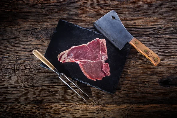 T-bone stek z wołowiny. Surowa wołowina stek T-bone na łupków płyta rzeźnik zioła sól pieprz i widelec — Zdjęcie stockowe