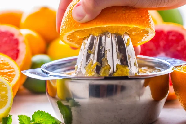 Preparation of orange grape or multivitamin juice, hands squeeze juice on a manual metal juicer surrounded by fresh tropical fruit — Stock Photo, Image