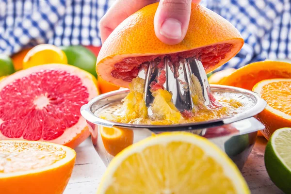 Preparación de uva de naranja o jugo multivitamínico, manos exprimen jugo en un exprimidor manual de metal rodeado de frutas tropicales frescas — Foto de Stock