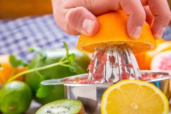 Preparation of orange grape or multivitamin juice, hands squeeze juice on a manual metal juicer surrounded by fresh tropical fruit — Stock Photo, Image