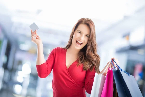 Hermosa chica feliz con tarjeta de crédito y bolsas de compras en la tienda — Foto de Stock