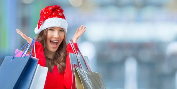 Julhandeln. Attraktiva glad tjej med kreditkort och kassar i santa hatt — Stockfoto