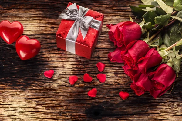 Ημέρα του Αγίου Βαλεντίνου γάμου έννοια. Μπουκέτο με τριαντάφυλλα και τυλιγμένο δώρο με κόκκινες καρδιές στο ξύλινο τραπέζι — Φωτογραφία Αρχείου