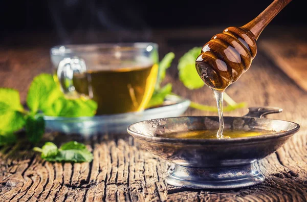 ¿Cariño? Cuchara de miel y miel en una mesa de roble rústico. Té caliente de hierbas en el fondo —  Fotos de Stock