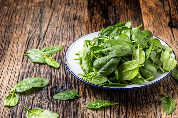 Spinach. Fresh baby spinach leaves in plate on woden table