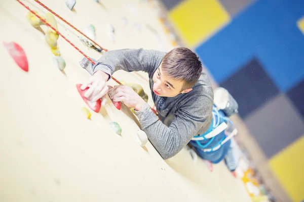 Escalade sur mur.Jeune homme pratiquant l'escalade sur un mur de roche à l'intérieur — Photo