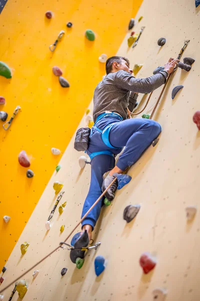 Klättrare på väggen. Ung man öva klättring på en rock-vägg inomhus — Stockfoto