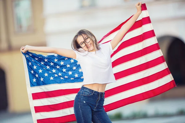 Happy young american school girl holding and waving in the city with USA flag