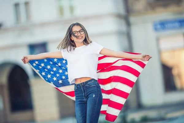 Happy young american school girl holding and waving in the city with USA flag — Stock Photo, Image