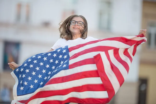 Happy young american school girl holding and waving in the city with USA flag