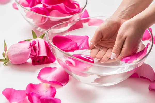 Manos femeninas y tazón de agua de spa con rosas rosadas y pétalos —  Fotos de Stock