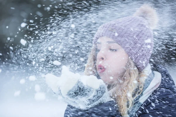 Beautiful young woman in warm clothing blowing snow — 스톡 사진