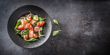 Koyu mutfak masasında sebzeli somon salatası.