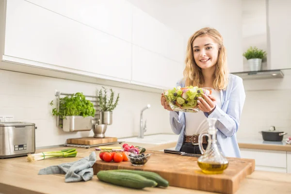 Joven chica rubia feliz preparando ensalada saludable en la cocina casera —  Fotos de Stock