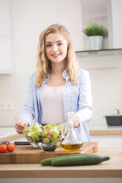 Joven chica rubia feliz preparando ensalada saludable en la cocina casera —  Fotos de Stock