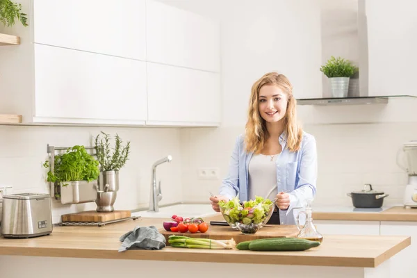 Giovane ragazza bionda felice preparare insalata sana in cucina di casa — Foto Stock