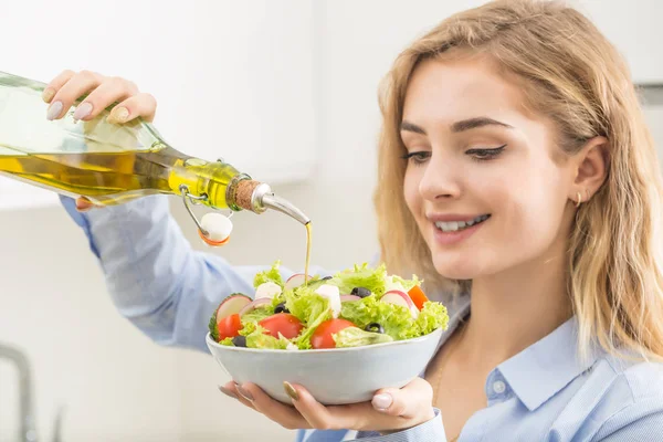 Junge Frau gießt Olivenöl in den Salat. Gesunder Lebensstil — Stockfoto