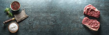 Eskimiş iki çiğ biftek et satırı ve koyu beton arka planda tuz biberi panoramik afiş