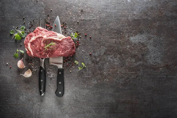 Filete de res crudo con tenedor y cuchillo sal pimienta y hierbas sobre fondo de hormigón oscuro — Foto de Stock
