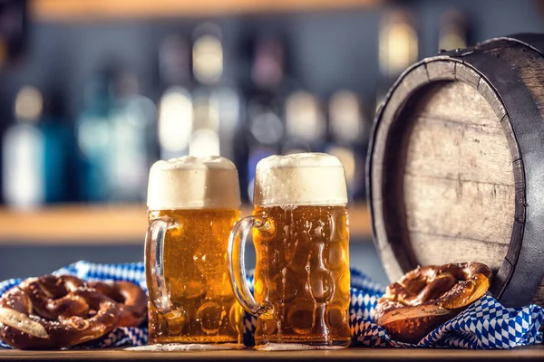 Oktoberfest duas grandes cervejas com pretzel barril de madeira e toalha de mesa azul — Fotografia de Stock