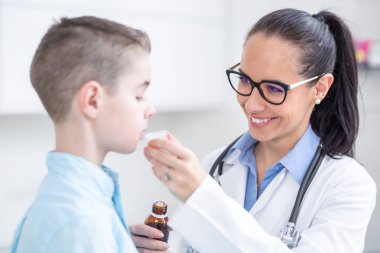 Pediyatrist kadın doktor, yavruya bir doz öksürük şurubu veriyor.