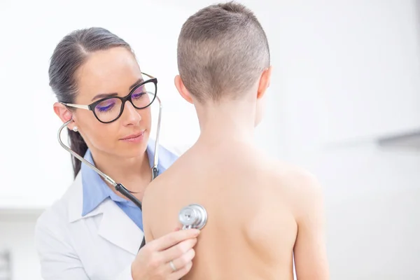 Jonge vrouwelijke arts kinderarts onderzoekt jongen patiënt met steth — Stockfoto