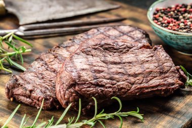 İki biftek, ot, domates, tuz ve baharat kasap tahtasında.