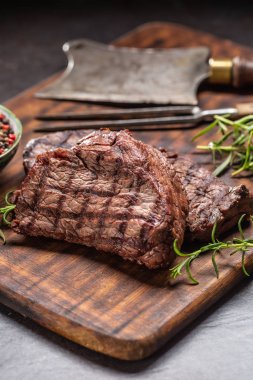 İki biftek, ot, domates, tuz ve baharat kasap tahtasında.