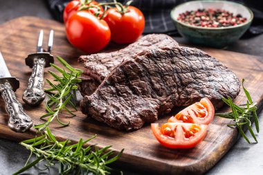 İki biftek, ot, domates, tuz ve baharat kasap tahtasında.