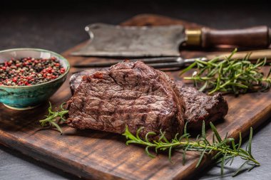 İki biftek, ot, domates, tuz ve baharat kasap tahtasında.