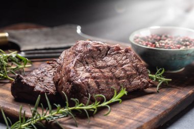 İki biftek, ot, domates, tuz ve baharat kasap tahtasında.