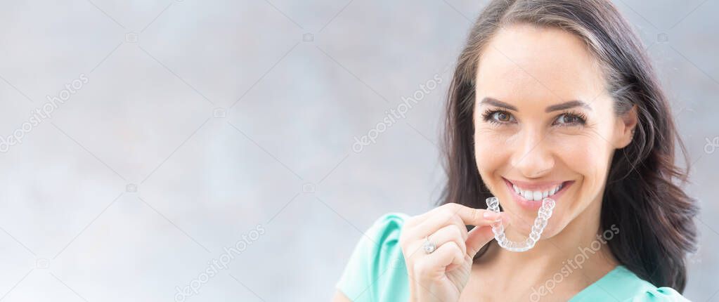 Invisalign orthodontics concept - Young attractive woman holding - using invisible braces or trainer.