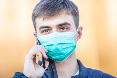 Yüzünde koruyucu maske olan genç adam cep telefonundan iletişim kuruyor. Coronavirus Covid-19 konsepti.
