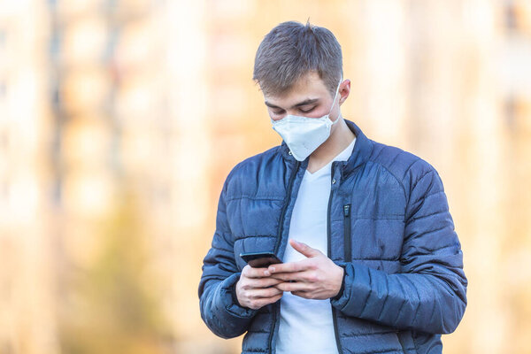 Young man with protective mask on his face communicates from mobile phone. Coronavirus Covid-19 concept.