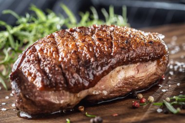 Ahşap tahtada, tuzlu baharat ve biberiyeli kızarmış ördek göğsü.