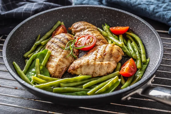 Friska recept på grillad kyckling, gröna grönsaker och tomater på en mörk nonstick pan placeras på metallisk rutnät och mörk bakgrund — Stockfoto