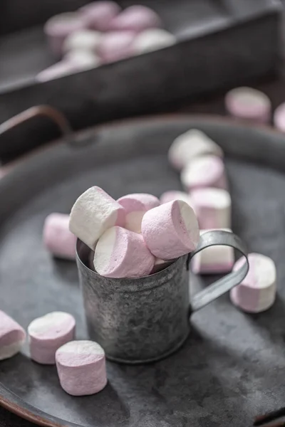 Potret dekat nampan logam vintage, permukaan dan cangkir dengan marshmallow merah muda dan putih di dalam cangkir dan tersebar di sekitar nampan serta di kotak logam di latar belakang — Stok Foto