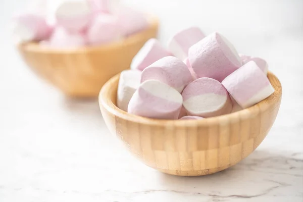 Rosa och vita marshmallows i en full träskål placerad på en marmoryta med fokus på skålen framtill — Stockfoto